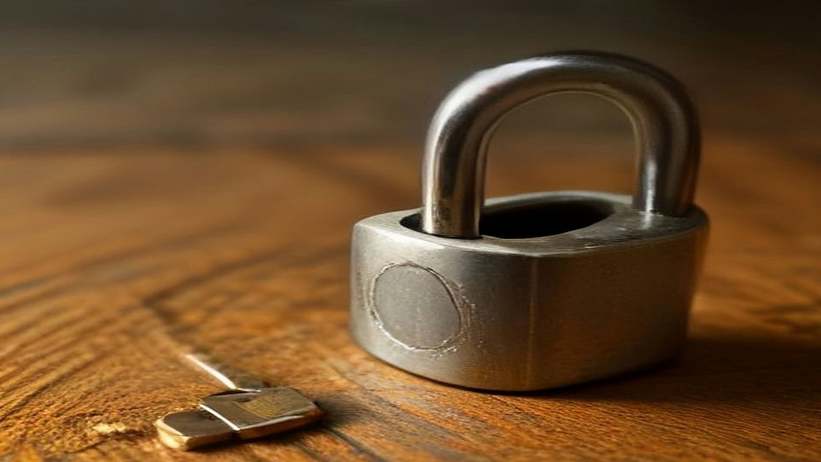 A steel padlock and a small key on a wooden table, representing locked-down session cookies